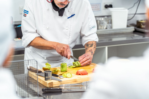 Male chef cutting kiwifruit with a knife on a chopping board.